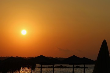 ciel jaune orangé au coucher de soleil au dessus d'une plage et ses parasols en paille en contre jour