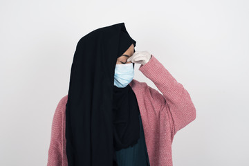 Very upset, Muslim woman wearing face mask touching nose between closed eyes, wants to cry, having...