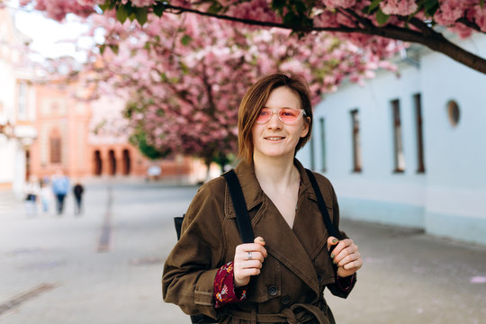 Happy travel woman with backpack and pink sunglass. Sakura cherry blossoms tree on background. Vacation, hanami concept 