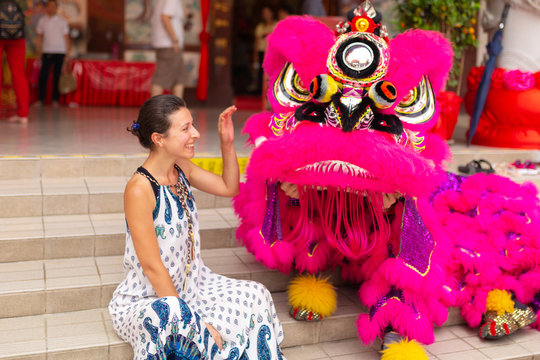 A European tourist girl at a Chinese New Year celebration in a Chinese temple is photographed with a traditional Chinese dragon. Festive Chinese entertainment