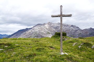 Cross on top of the mountains of Livigno Alps on the border between Italy and Switzerland, cloudy summer day, Italy