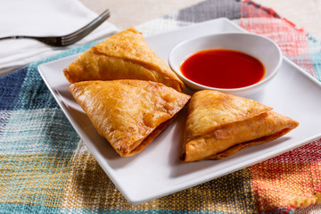 A view of a plate of three sambusa appetizers, in a restaurant or kitchen setting.