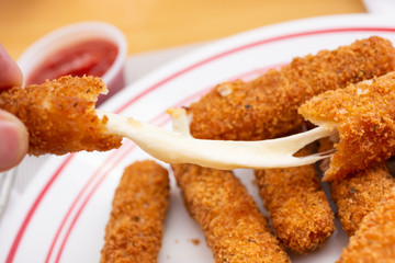 A closeup view of an appetizer plate of deep fried mozzarella sticks, with a hand pulling away the gooey cheese.