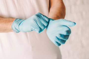 Closeup of professional doctor putting on blue latex gloves on hands. Man wearing sterile protective medical gloves on hands. Personal protection. Medical examination of patient. Coronavirus COVID-19