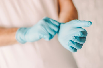 Closeup of man putting on medical protective gloves on hands. Professional doctor wearing sterile blue latex gloves on hands. Medical examination of coronavirus COVID-19 patient. Personal protection