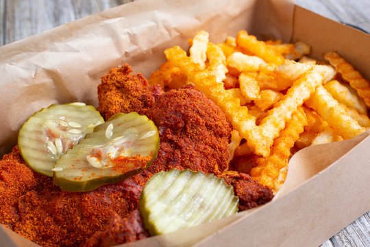 A View Of A Delivery Carton With Spicy Hot Chicken Tenders And Crinkle Cut French Fries, In A Restaurant Or Kitchen Setting.