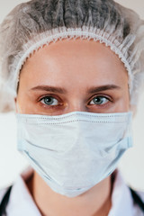 Head and shoulders portrait of female doctor wearing protective mask and looking at camera posing against white background, copy space