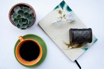 Taza de café con elementos decorativos, planta, libreta, bicicleta, baúl de madera sobre una superficie blanca