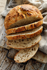 Homemade sourdough loaf of bread cut into slices on a wooden board, top view