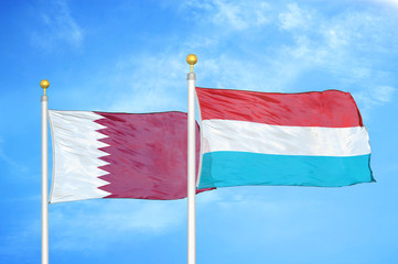 Qatar and Luxembourg two flags on flagpoles and blue cloudy sky