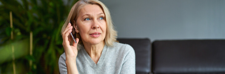 Beautiful mature blond woman talking on mobile phone at sofa.