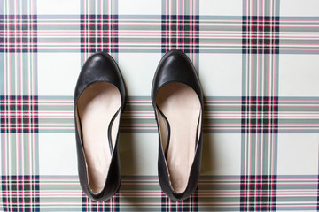 pair of black female shoes on checkered british fabric. free copy space. Overhead shot of elegant shoes. Top view. Concept of fashion.