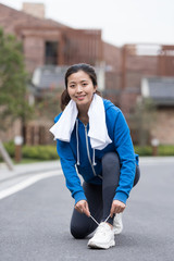 A young Asian woman squatting to tie shoelaces