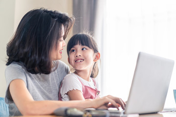 Fototapeta na wymiar Asian young mother work from home. Woman use laptop for meeting with colleague while daughter sit on the lap and smile. Mom happy to do job while taking care family. Covid-19 Social distancing concept