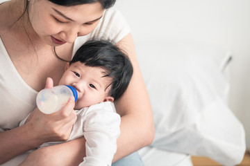 Obraz na płótnie Canvas Asian young woman hug, feed milk to cute infant baby boy. Son happy to stay and sleep in mom warm embrace. Infant drink nutrition food from mom. Mother child relationship for kid development concept.