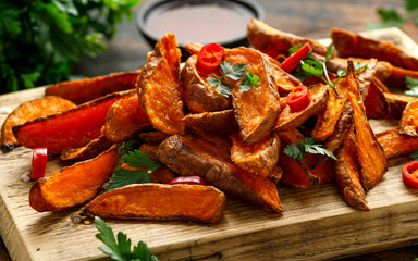 Healthy Baked Orange Sweet Potato wedges with dip sauce, herbs, salt and pepper on wooden board