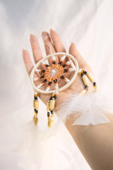 Dream catcher in female woman hand on satin, handmade native american of yellow blue beads with white feathers. Bad dreams protection. Concept peaceful, peace of mind, meditation, tranquility