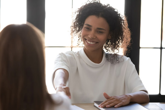Close up happy successful african american businesswoman shaking hand of applicant at interview. HR manager making good first impression. Employer congratulates attractive candidate getting hired.
