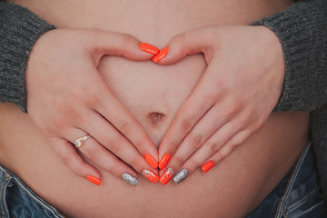 Young pregnant woman holding hands on her belly in the shape of a heart 