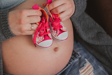 Young woman hands holding children shoes on a pregnant belly.