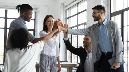 Excited successful multiracial business people with attractive mentor giving high five, celebrating...