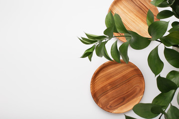 Wooden plates and green leaves on white background