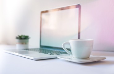 Cup of coffee with mockup laptop in background on work desk in sunset. Close-up cup of tea with morning light. Modern, thin laptop design. Isolated screen for mockup. Laptop profile. Home office