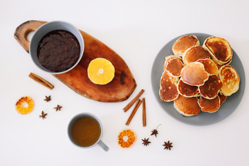 Lush pancakes and teapot with spices, cup of tea with orange, cinnamon, anise. Tasty breakfast on white background. Good morning