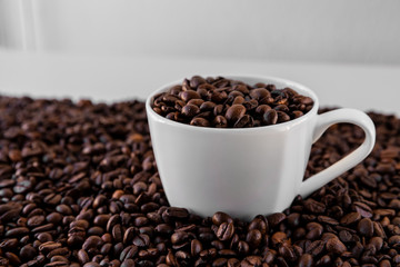 White mug with roasted coffee beans everywhere, inside the mug and a lot around it with white background. Great for going to a cafe, restaurant, cafeteria menu or as a sign.
