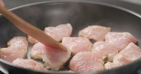 shot of frying turkey fillet pieces on nonstick pan and moving them with wood spatula