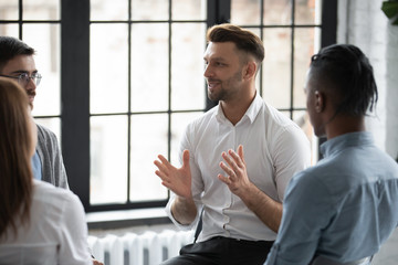 Happy male psychologist counselling speaking with diverse people sitting in circle at group therapy...