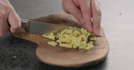 man hands chopping fresh ginger root with knife on olive wood board