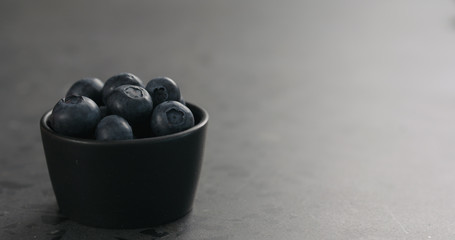 small black bowl with fresh blueberries on concrete surface with copy space