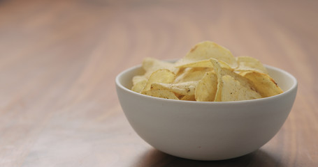 white bowl with black pepper seasoned potato chips on walnut wood table with copy space