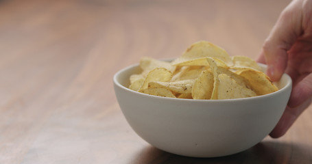 man hand bring white bowl with black pepper seasoned potato chips on walnut wood table with copy space