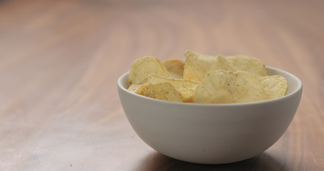 white bowl with black pepper seasoned potato chips on walnut wood table with copy space