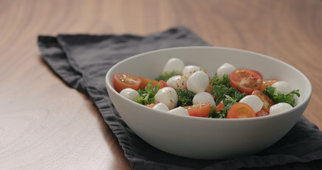 salad with kale , cherry tomatoes and mozzarella in white bowl