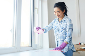 Waist up portrait of Smiling woman washing windows during Spring cleaning, focus on female hands wearing pink gloves, copy space