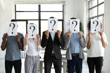 Diverse business people hiding faces behind papers sheets with question marks, standing in row in...