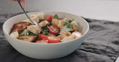 man tastes caesar salad with kale and turkey in white bowl