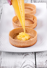 Shortbread tartlets are filled with lemon curd out of the pastry bag on the ceramic platter