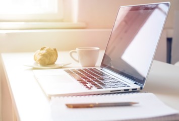 Laptop mockup on work desk in sunset. Close-up laptop with flowers, coffee, croissant, with morning light. Modern, thin laptop design.White. Isolated screen for mockup. Laptop profile. Home office
