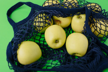 blue string bag with green apples on a green background
