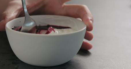 man hand mix bilberry juice with white yogurt in white bowl on concrete surface