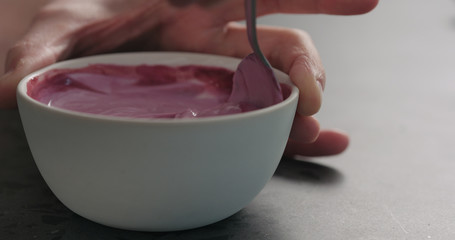 man hand mix bilberry juice with white yogurt in white bowl on concrete surface