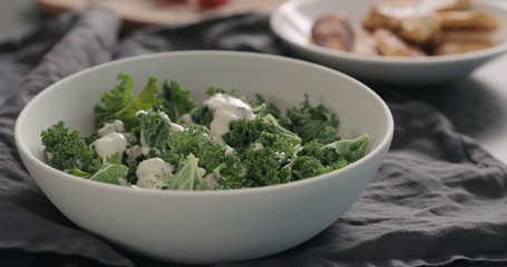 pour caesar dressing on kale leaves in white bowl