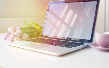 Laptop mockup on work desk in sunset. Close-up laptop with flowers, coffee, croissant, with morning light. Modern, thin laptop design.White. Isolated screen for mockup. Laptop profile. Home office