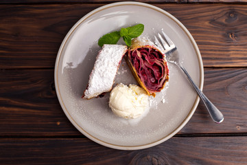 dessert of cherry strudel on a plate, wooden background, top view