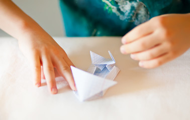 Children kid hands do origami on the white table.