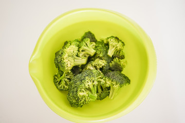 Top down shot of bright vibrant green bowl filled with ripe broccoli stems ready for delicious and healthy meal preparation